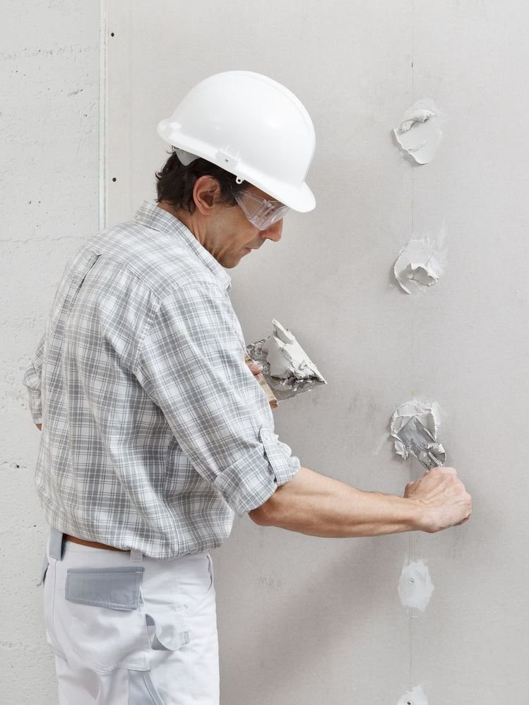 Un homme portant un casque et des lunettes de sécurité est en train de plâtrer un mur.