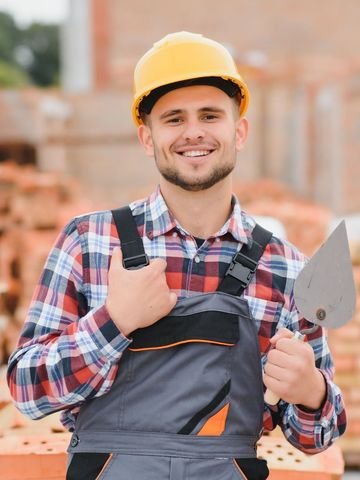 Un homme portant un casque et une salopette tient une truelle.